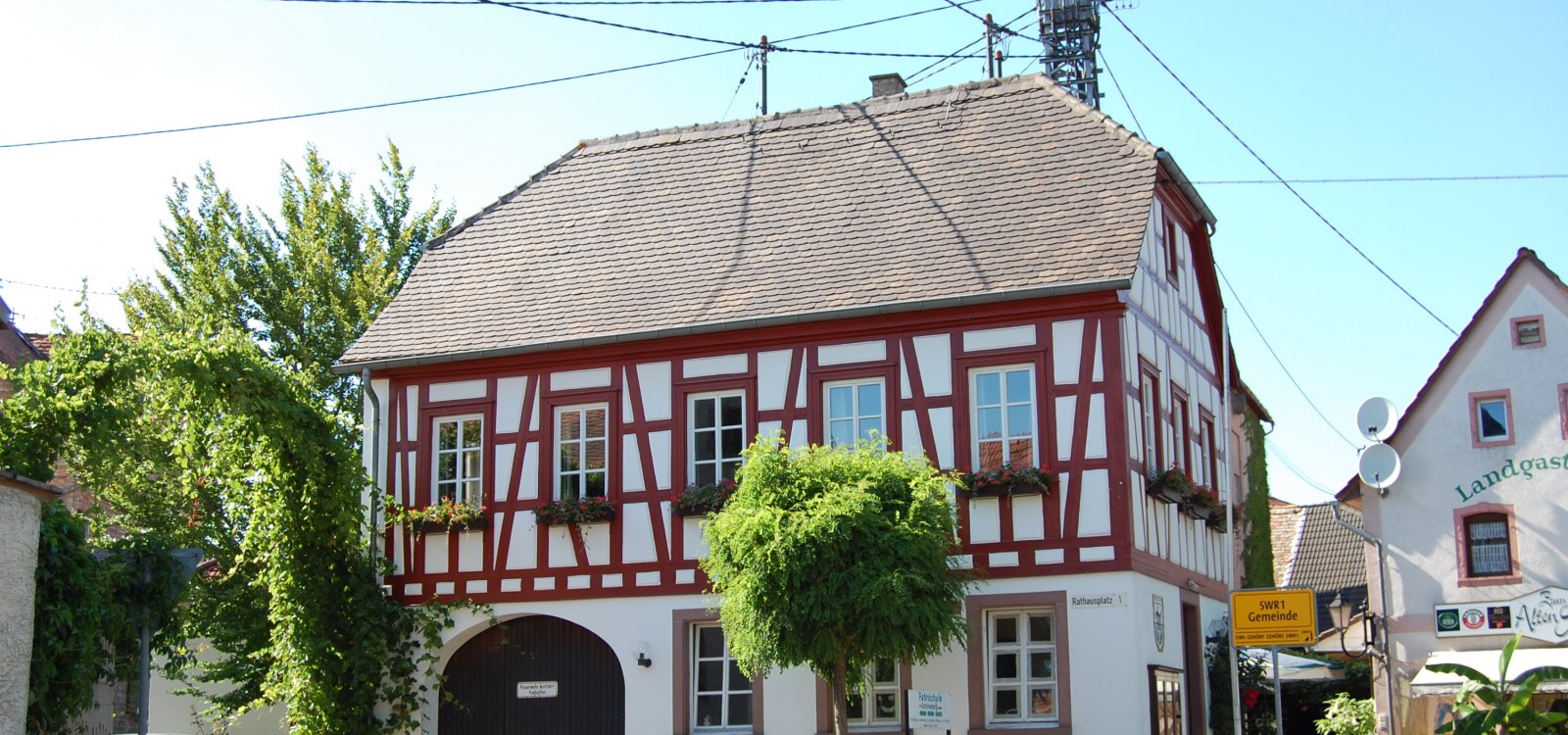 Das historische Rathaus in der Ortsmitte von Uelversheim, © Rhein-Selz Tourismus e. V. Fachwerkhaus an einer Straßenecke, umgeben von Bäumen und weiteren Gebäuden