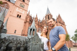 Ein Paar steht vor der Oppenheimer Katharinenkirche und schaut sich die Details der Modellkirche aus Bronze an., © Dominik Ketz, Rheinhessen-Touristik GmbH Paar steht vor der Katharinenkirche und betrachtet ein Modell der gotischen Kirche