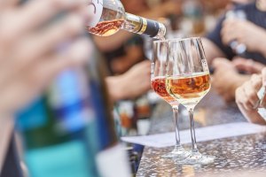 Wein ausschenken, © Robert Dieth und Iris Schröder Wein wird in zwei Weingläser an einem Tisch mit mehreren Personen im Hintergrund eingeschenkt