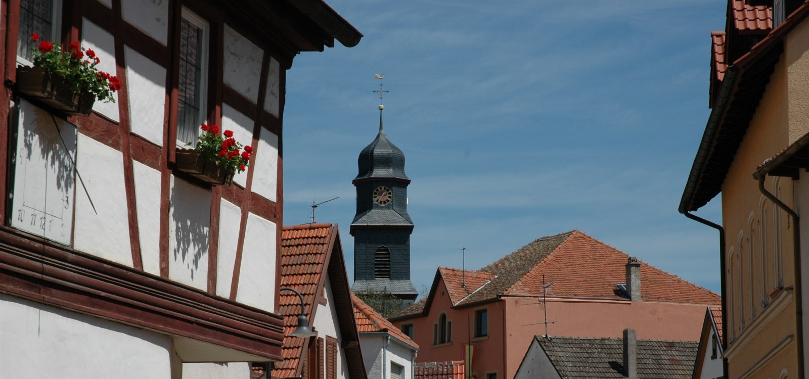 Dolgesheim, © Rhein-Selz Tourismus e. V. Blick auf eine Straße mit Fachwerkhäusern und einem Kirchturm im Hintergrund.
