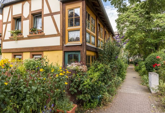 Promenade Guntersblum, © Achim Meurer Fachwerkhaus mit Blumenbeeten an einem Gehweg, umgeben von Bäumen und Sträuchern