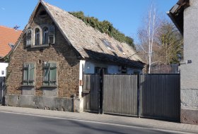 Altes Backsteinhaus mit schr&auml;gem Dach und Fensterl&auml;den, daneben ein hohes Holztor