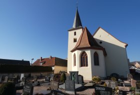 Kirche mit spitzem Turm und Friedhof mit Grabsteinen bei klarem Himmel