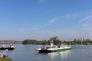 F&auml;hre auf einem Fluss bei klarem Himmel, Ufer mit Gras und B&auml;umen im Hintergrund