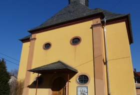 Gelbes Kirchengeb&auml;ude mit kleinem Turm und Schieferdach vor blauem Himmel