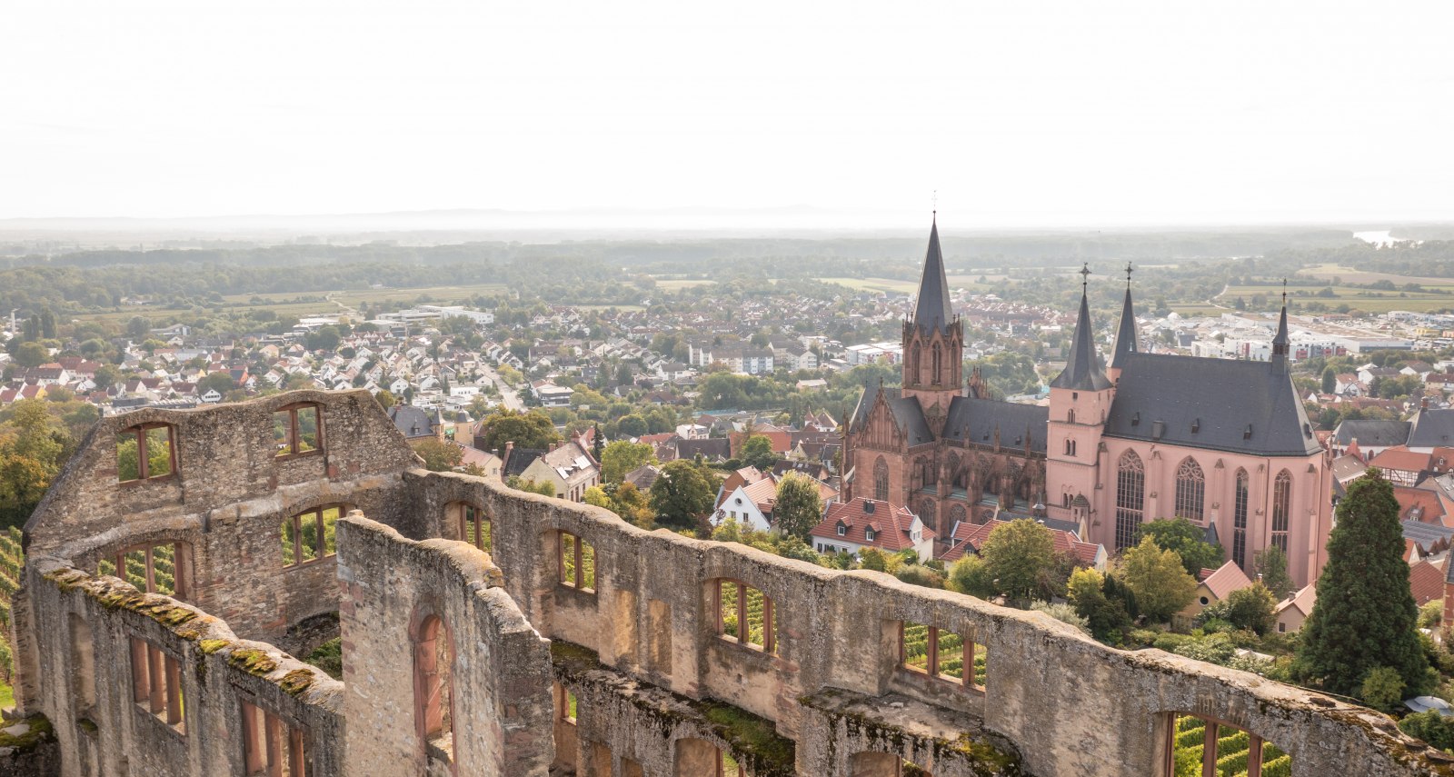 Luftaufnahme von einer Burgruine, eine Kirche und Stadt im Hintergrund