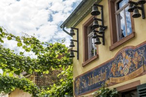 Fassade des Gasthauses St. Urbanshof mit Glocken und Wandmalerei
