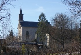 Kirche mit spitzem Turm hinter kahlen B&auml;umen an einem klaren Wintertag