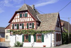 Fachwerkhaus mit gr&uuml;n lackierten Fensterl&auml;den und Weinreben an der Fassade unter blauem Himmel