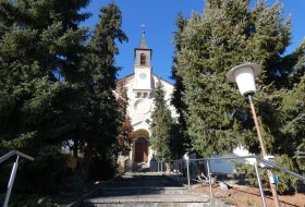 Eine Treppe f&uuml;hrt zum Eingang einer Kirche, seitlich sind hohe Tannen.
