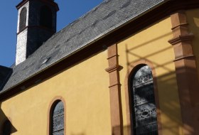 Gelbes Kirchengeb&auml;ude mit Kirchturm und Schieferdach unter klarem blauem Himmel