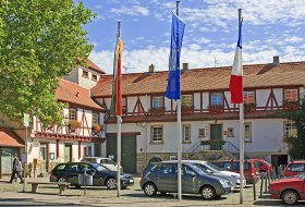 Zentraler Platz mit Fachwerkh&auml;usern, parkenden Autos und drei Fahnenmasten mit Flaggen