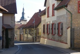 Enge Stra&szlig;e in einem Dorf mit Fachwerkh&auml;usern und einem Kirchturm im Hintergrund