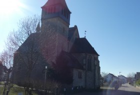 Kirche mit hohem spitzem Turm bei sonnigem Himmel, Schatten auf gepflastertem Weg