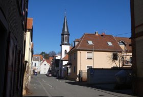 Stra&szlig;e in einem kleinen Ort mit Wohnh&auml;usern und einem Kirchturm unter klarem blauem Himmel