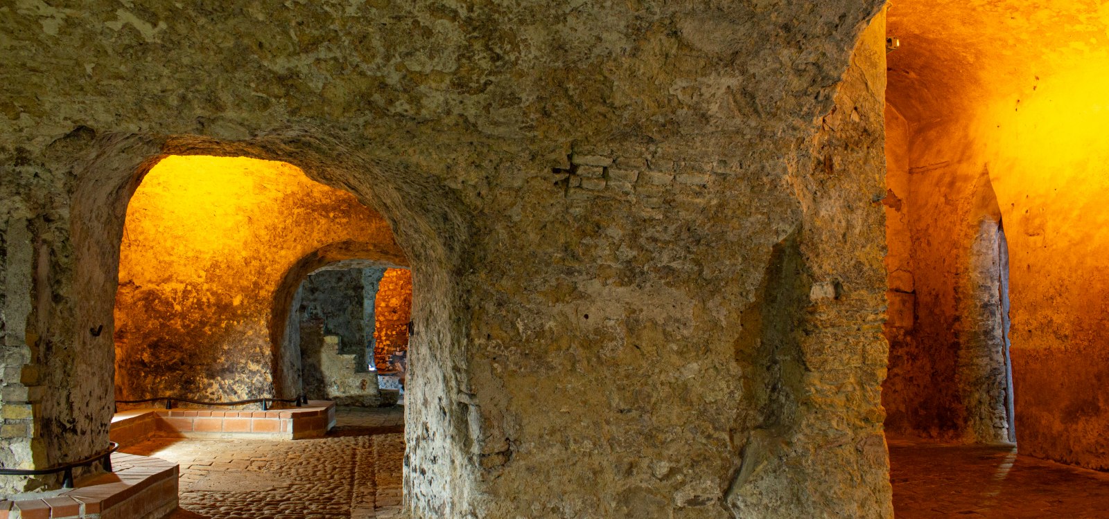 Beleuchteter unterirdischer Gew&ouml;lberaum mit groben Steinw&auml;nden und B&ouml;gen