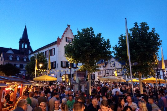 Belebter Marktplatz bei Abenddämmerung mit vielen Menschen, historischen Fachwerkhäusern und beleuchteten Ständen