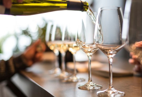 Wei&szlig;wein wird aus einer Weinflasche in ein Weinglas an einem gedeckten Tisch eingeschenkt