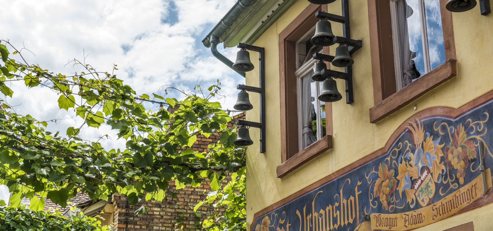 Fassade des Gasthauses St. Urbanshof mit Glocken und Wandmalerei
