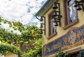 Fassade des Gasthauses St. Urbanshof mit Glocken und Wandmalerei