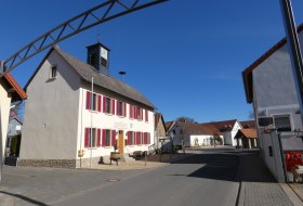 Wei&szlig;es Rathausgeb&auml;ude mit roten Fensterl&auml;den und kleinem Glockenturm an sonnigem Tag in einer Dorfstra&szlig;e