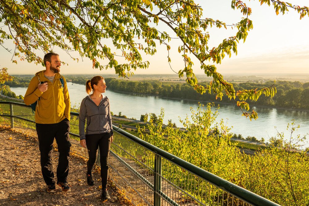 Ein Paar wandert und blickt auf die herbstliche Landschaft und einen Fluss.