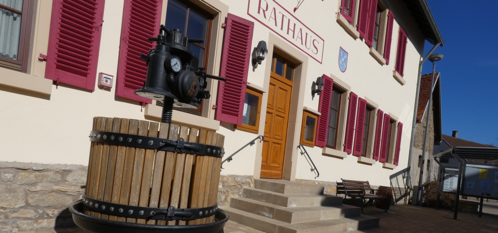 Eingang mit Treppen zum Rathausgebäude, davor eine historische Weinpresse