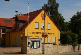 Gelbes Gebäude mit rotem Dach, davor eine Steinmauer