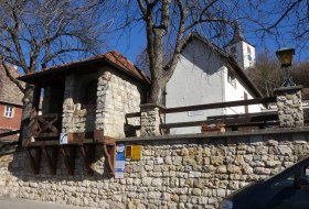 Steinerne Mauer mit &uuml;berdachtem Aussichtspunkt und dahinter eine wei&szlig;e Kirche mit Turm
