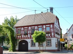 Fachwerkhaus an einer Straßenecke, umgeben von Bäumen und weiteren Gebäuden