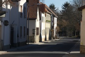 Sonnige, ruhige Stra&szlig;e mit Reihenh&auml;usern und B&auml;umen im Hintergrund