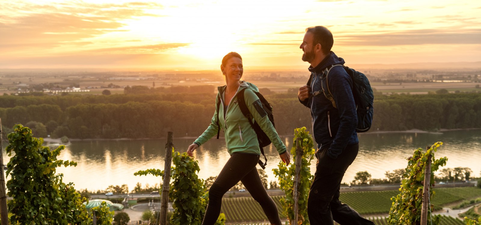 Ein Paar wandert bei Sonnenuntergang durch die Weinberge mit Blick auf einen Fluss.