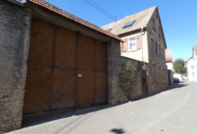 Altes Haus mit gro&szlig;en h&ouml;lzernen Doppeltoren an einer ruhigen Stra&szlig;e bei klarem Himmel