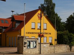 Gelbes Gebäude mit rotem Dach, davor eine Steinmauer