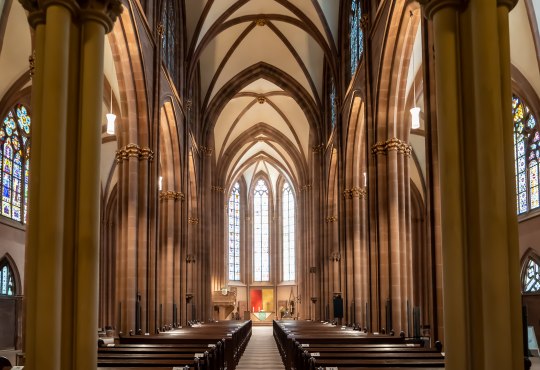 Innenraum einer gotischen Kirche mit hohen Spitzbögen, Säulen und bunten Glasfenstern,