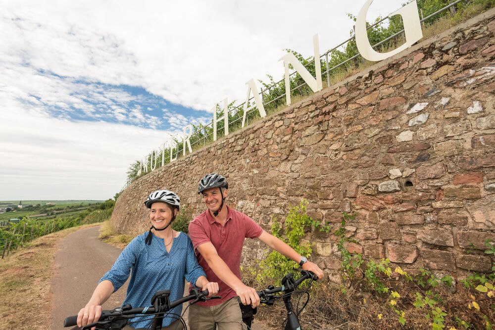 Zwei Radfahrer sind in den Weinbergen unterwegs. &Uuml;ber ihnen der Schriftzug Roter Hang