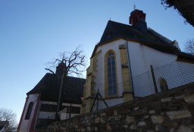 Blick auf eine Kirche mit hohen Fenstern, umgeben von einer Steinmauer und einem Zaun, vor klarem Himmel