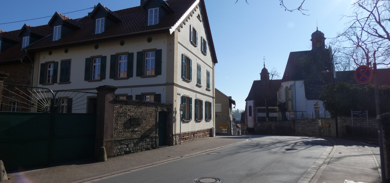 Stra&szlig;e mit altem Haus links und Kirche im Hintergrund bei sonnigem Himmel