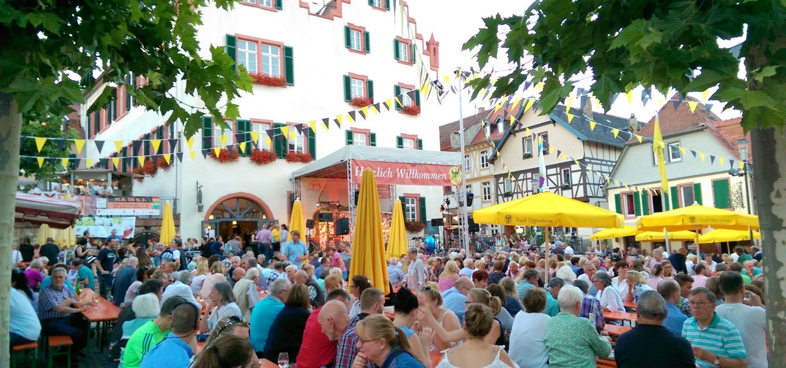 Menschen sitzen an Tischen bei einem Fest vor historischen Fachwerkhäusern